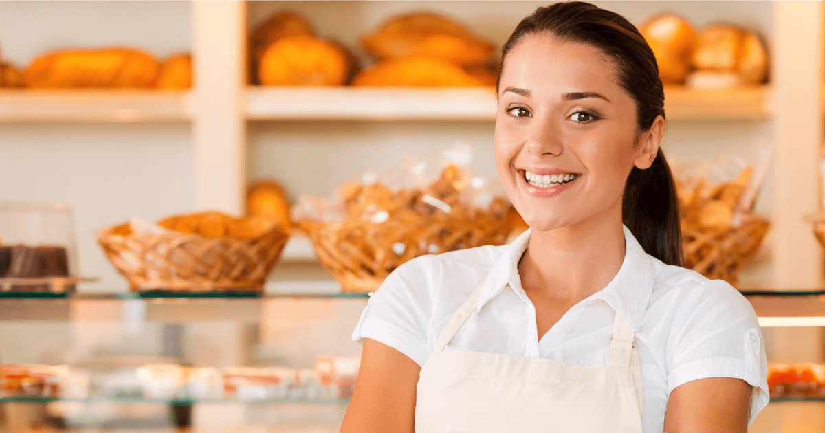 Beautiful young woman in apron keeping arms crossed while standing in bakery shop