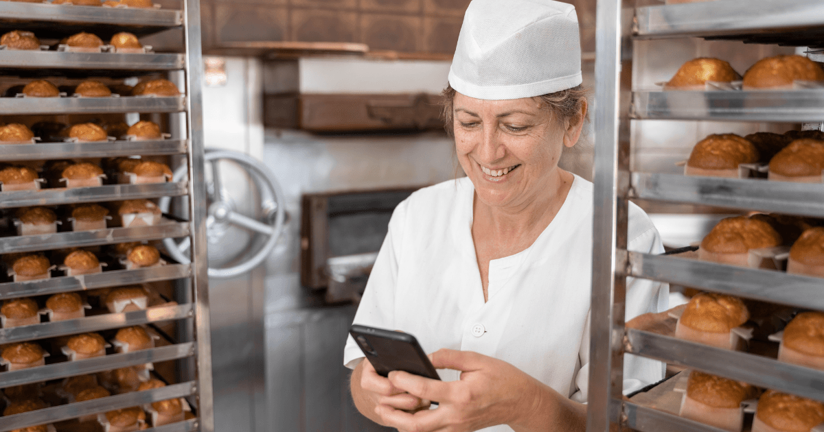 Baker woman smiling and texting with her phone surrounded by fresh baked cupcakes